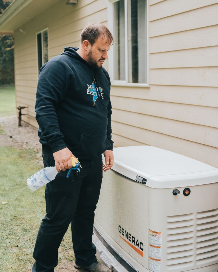 Ricky Mauro in a Mauro Electric hoodie beside a Generac standby generator installed against the side of a house